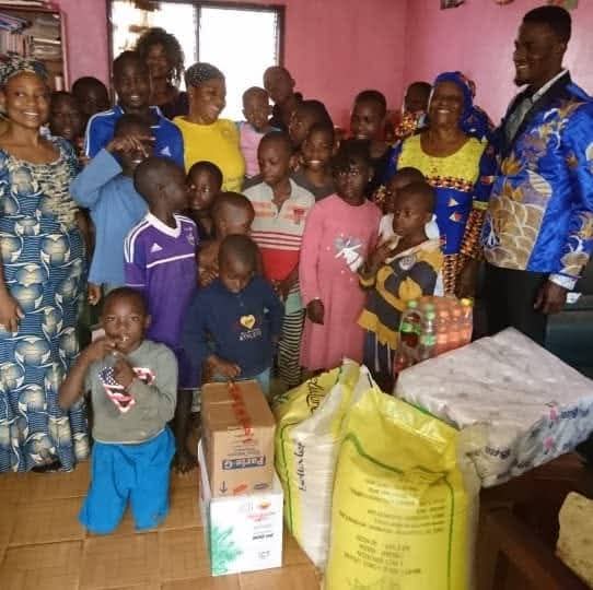 Prophet Emmanuel Ayuh and church members with children at an orphanage in Yaoundé, beside donated rice, drinks and household supplies.